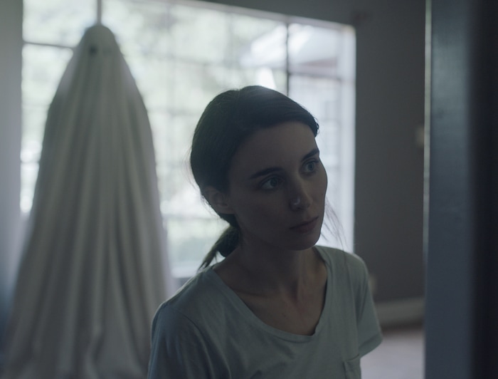 This image released by A24 shows Rooney Mara and Casey Affleck in a scene from the film, "A Ghost Story." Affleck plays the ghost in the new David Lowery film. For most of the movie he’s silent and cloaked in a white sheet with eye holes as he returns to his home to look in on his still-living partner played by Mara.  (Bret Curry/A24 via AP)