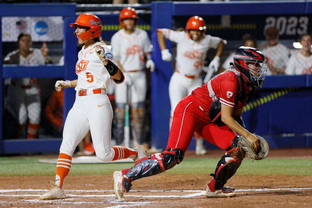 Oklahoma State's Kiley Naomi (5) scores past Utah catcher Kendall Lundberg, right, during the first inning of an NCAA softball Women's College World Series game Friday, June 2, 2023, in Oklahoma City. (AP Photo/Nate Billings)