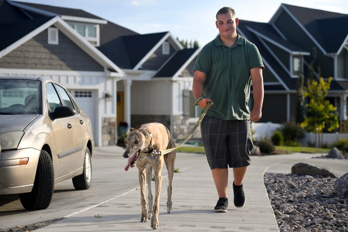 ADVANCE FOR WEEKEND EDITIONS - In this Aug. 16, 2017, photo, Gage Bowls walks his aunt's dog, Andy, a Greyhound, in the Bowls' neighborhood in Spanish Fork, Utah. At birth, Bowls suffered four hours of oxygen depravation which left him with mental and physical deficiencies, including cerebral palsy. (Isaac Hale/The Daily Herald via AP)