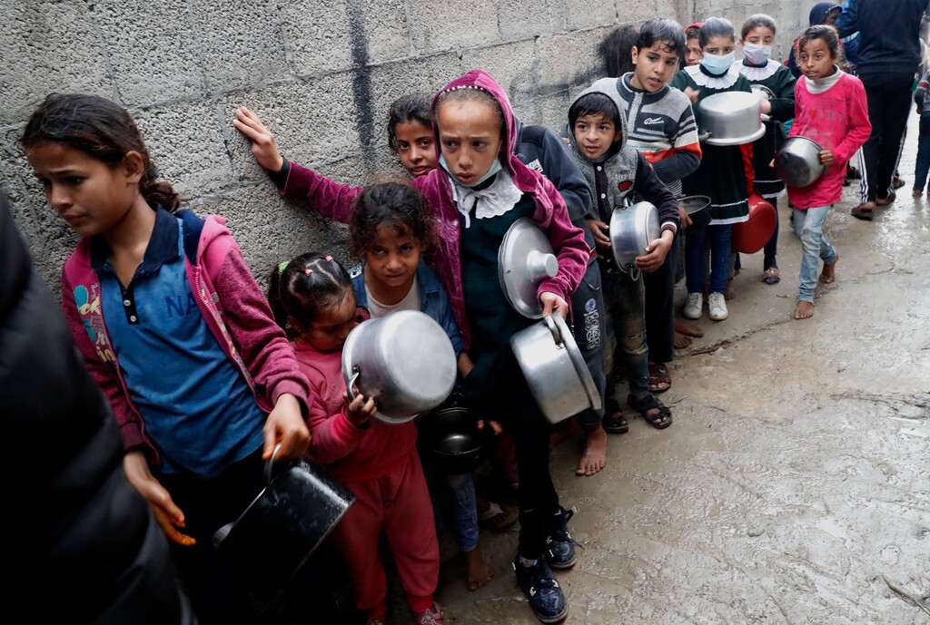 Palestinian children wait in line while holding pots to receive free meals of green pea stew cooked by Samera Abu Amra, unseen,  for distribution to poor residents in Gaza City, Feb. 4, 2021. Amra cooks the meals with money sent by benefactors to help feed the poor as poverty and unemployment rates in Gaza hover around 50%. (AP Photo/Adel Hana)