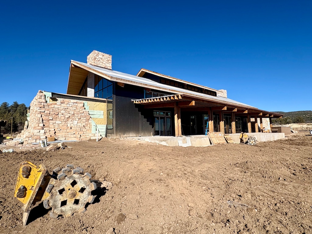 A stone and wood building under construction rises in front of a brown dirt field. Construction equipment sits in the foreground.
