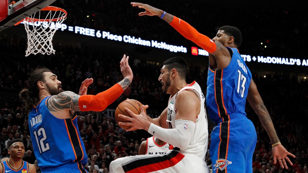 Portland Trail Blazers center Enes Kanter, center, grabs a rebound as Oklahoma City Thunder center Steven Adams, front left, and Thunder forward Paul George, right, defend during the second half of Game 1 of a first-round NBA basketball playoff series in Portland, Ore., Sunday, April 14, 2019. (AP Photo/Steve Dipaola)