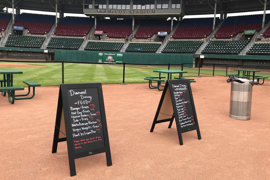 Menu boards and tables occupy the third base infield dirt in preparation for dining guests at McCoy Stadium, home of the Pawtucket Red Sox, in Pawtucket, Rhode Island, Wednesday, May 27, 2020. With the minor league baseball season on hold due to the coronavirus pandemic, the Triple-A affiliate of the Boston Red Sox had found another use for its home field. Starting next weekend, “Dining on the Diamond” will allow PawSox fans and others just longing for a taste of baseball to sample typical ballpark fare on the McCoy Stadium infield.(AP Photo/Jimmy Golen)