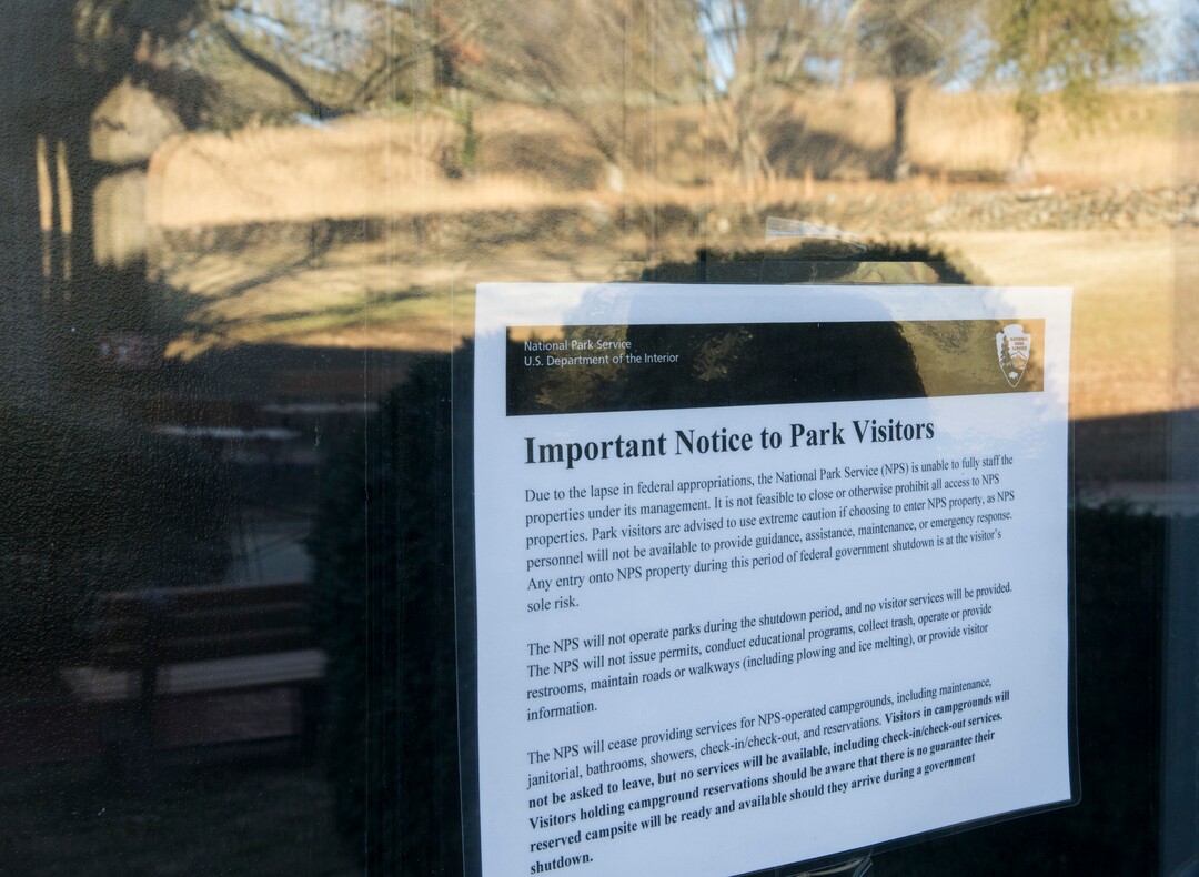 A sign is posted at the Fredericksburg and Spotsylvania National Military Park in Fredericksburg, Va. on Saturday,  Jan. 20, 2018 advising visitors that some services would be unavailable due to a government shutdown.  Reflected in the window is the Sunken Road, the site of fierce fighting during the Battle of Fredericskburg in 1862.  (Mike Morones/The Free Lance-Star via AP)