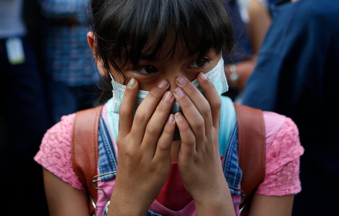 A girl wearing a dust mask covers her face as she watches rescuers work to save people believed to be still alive inside a collapsed office building in the Roma Norte neighborhood of Mexico City, Sept. 22, 2017, three days after a 7.1 magnitude earthquake. Hope mixed with fear Friday as families awaited word of their loved ones trapped in rubble. (AP Photo/Rebecca Blackwell)