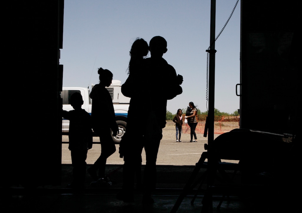 In this Wednesday, May 22, 2019, migrants mainly from Central America guide their children through the entrance of a World War II-era bomber hanger in Deming, N.M. A surge of asylum-seeking families has been straining cities along the southern U.S. border for months, but now the issue is flowing into cities far from Mexico, where immigrants are being housed in an airplane hangar and rodeo fairgrounds and local authorities are struggling to keep up with the influx. (AP Photo/Cedar Attanasio)
