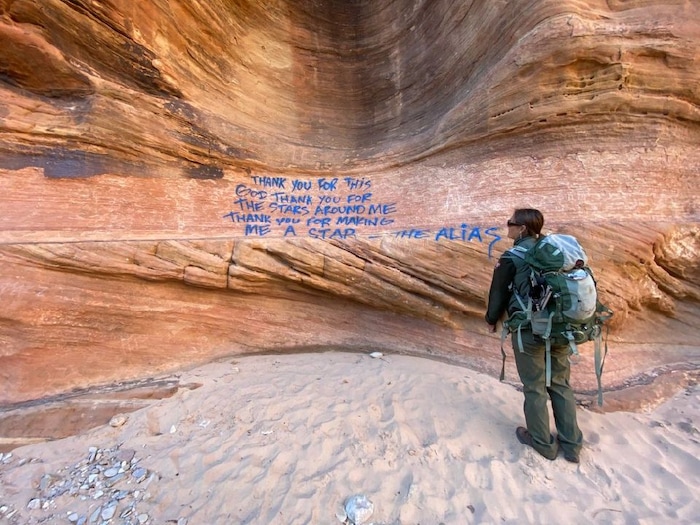 (Photo courtesy of the National Park Service) A ranger looks at a sandstone wall with blue spray paint graffiti at Zion National Park.