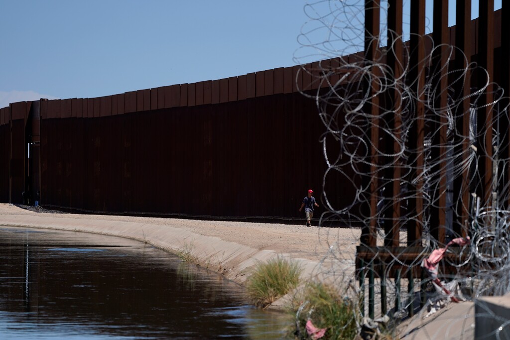 (Gregory Bull | AP) A man walks between a canal carrying water from the Colorado River and a border wall separating San Luis Rio Colorado, Mexico with San Luis, Ariz., on Sunday, Aug. 14, 2022, in San Luis Rio Colorado, Mexico.