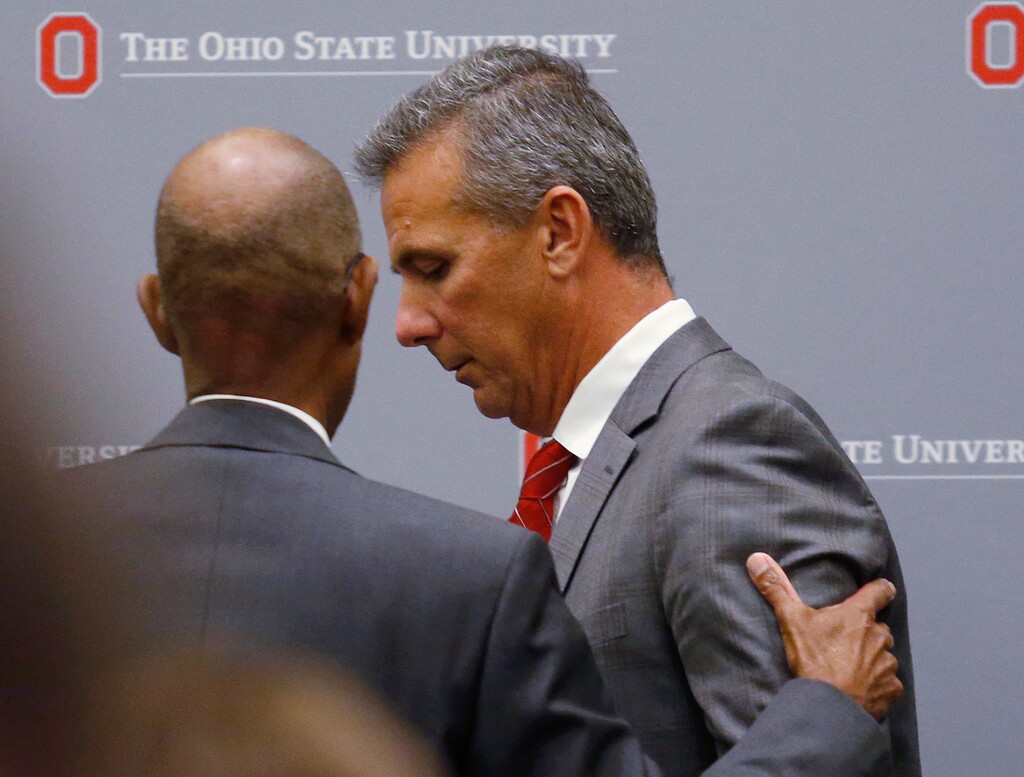 (AP Photo/Paul Vernon) Ohio State University President Michael Drake offers words to football coach Urban Meyer, who leaves the stage following a news conference in Columbus, Ohio, Wednesday, Aug. 22, 2018. Ohio State suspended Meyer on Wednesday for three games for mishandling domestic violence accusations, punishing one of the sport's most prominent leaders for keeping an assistant on staff for several years after the coach's wife accused him of abuse. Athletic director Gene Smith was suspended from Aug. 31 through Sept. 16.