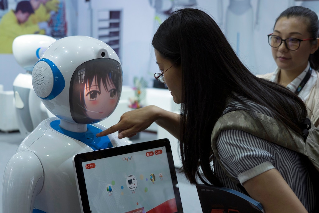 Women interact near a robot designed by Chinese robotics company Pangolin at the Consumer Electronics Show Asia 2018 in Shanghai, China on Friday, June 15, 2018. President Donald Trump is hiking the price of Chinese-made forklift trucks and X-ray machines for American buyers. They are part of a $50 billion list of Chinese exports targeted for a 25 percent tariff hike in response to complaints Beijing steals or pressures foreign companies to hand over technology. (AP Photo/Sam McNeil)