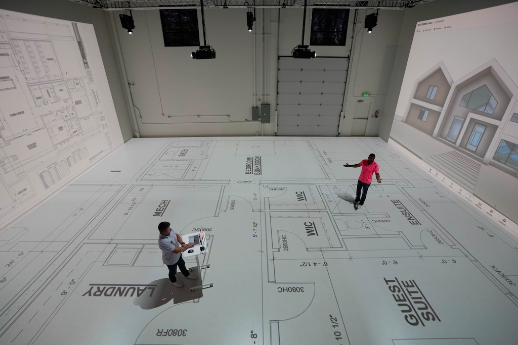 (Francisco Kjolseth | The Salt Lake Tribune) Nathan Christensen, left, and Trevor Pyne of Walk Your Plans navigate a house floor plan in their Lehi warehouse with the use of eight projectors on Wednesday, Sept. 10, 2025. The walkable projections allow clients to physically navigate future spaces to scale before construction begins. 