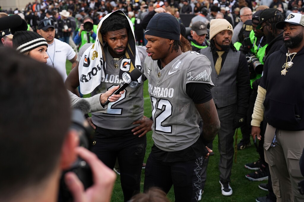 Colorado wide receiver Travis Hunter (12) answers a question during a television interview as Colorado quarterback Shedeur Sanders (2) listens after an NCAA college football game Saturday, Nov. 16, 2024, in Boulder, Colo. (AP Photo/David Zalubowski)