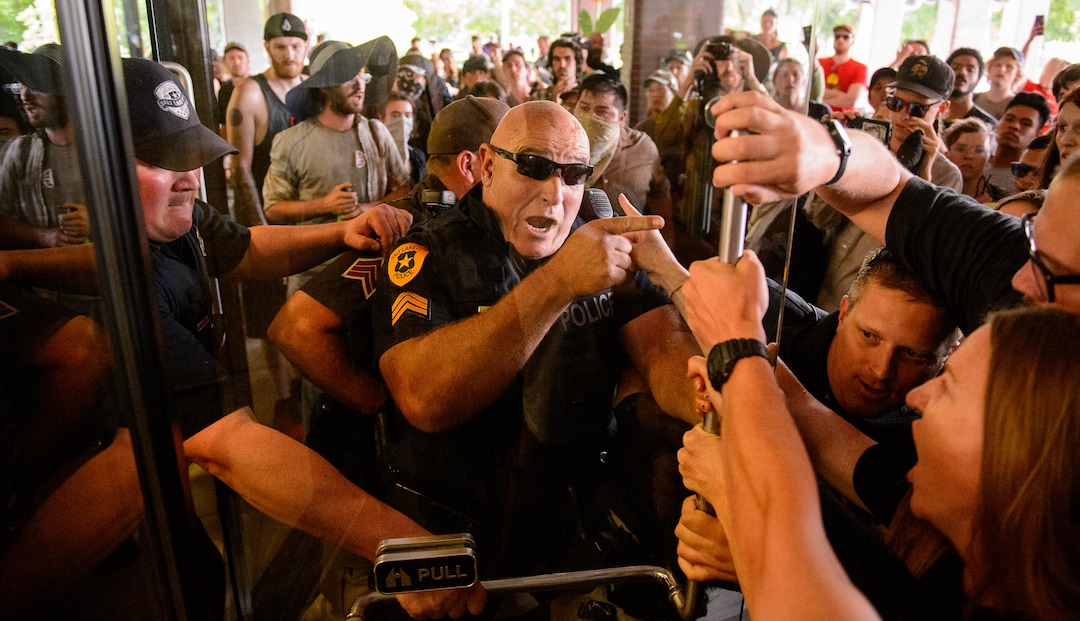 (Trent Nelson | The Salt Lake Tribune) Police struggle with protesters for control of a door at the Chamber of Commerce Building Salt Lake City on Tuesday, July 9, 2019. Dozens of people showed up to protest the proposed Inland Port and ended up clashing with police, resulting in temporary street closures and arrests.