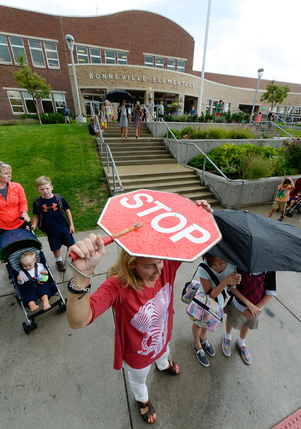 (Francisco Kjolseth | The Salt Lake Tribune) Julie Pereira, who works the front desk at Bonneville Elementary in Salt Lake shields herself from the rain as she plays double duty as a crossing guard following the first day of school. The school had just been informed that their crossing guards had resigned.