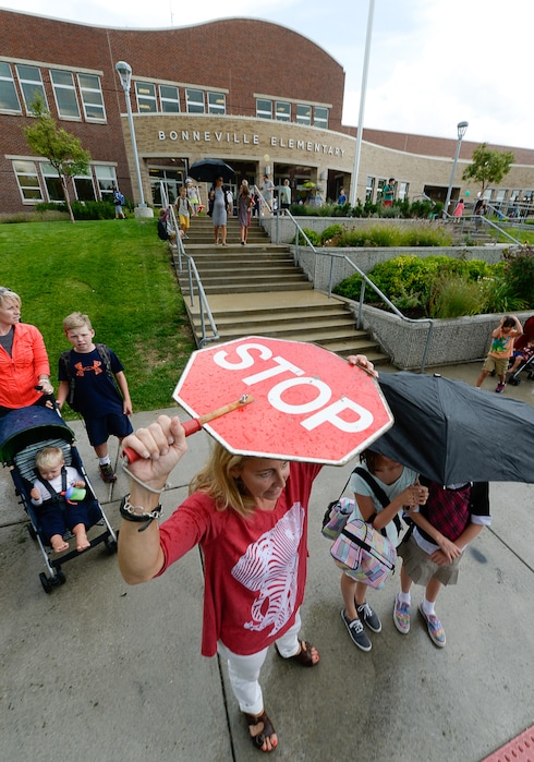 (Francisco Kjolseth | The Salt Lake Tribune) Julie Pereira, who works the front desk at Bonneville Elementary in Salt Lake shields herself from the rain as she plays double duty as a crossing guard following the first day of school. The school had just been informed that their crossing guards had resigned.