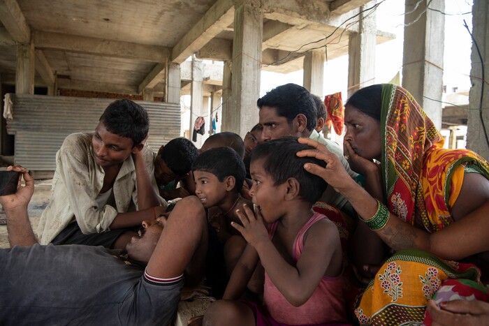 (Saumya Khandelwal | The New York Times) Rabita, right, and other villagers watch a wrestling match on a phone, inside the construction site where she works and lives in Lucknow, India, July 28, 2020. Around the world, the poor and marginalized are much more likely to be vulnerable to extreme heat; Rabita and her husband are Dalits, at the bottom of the Hindu caste ladder, working to pay off their debts.
