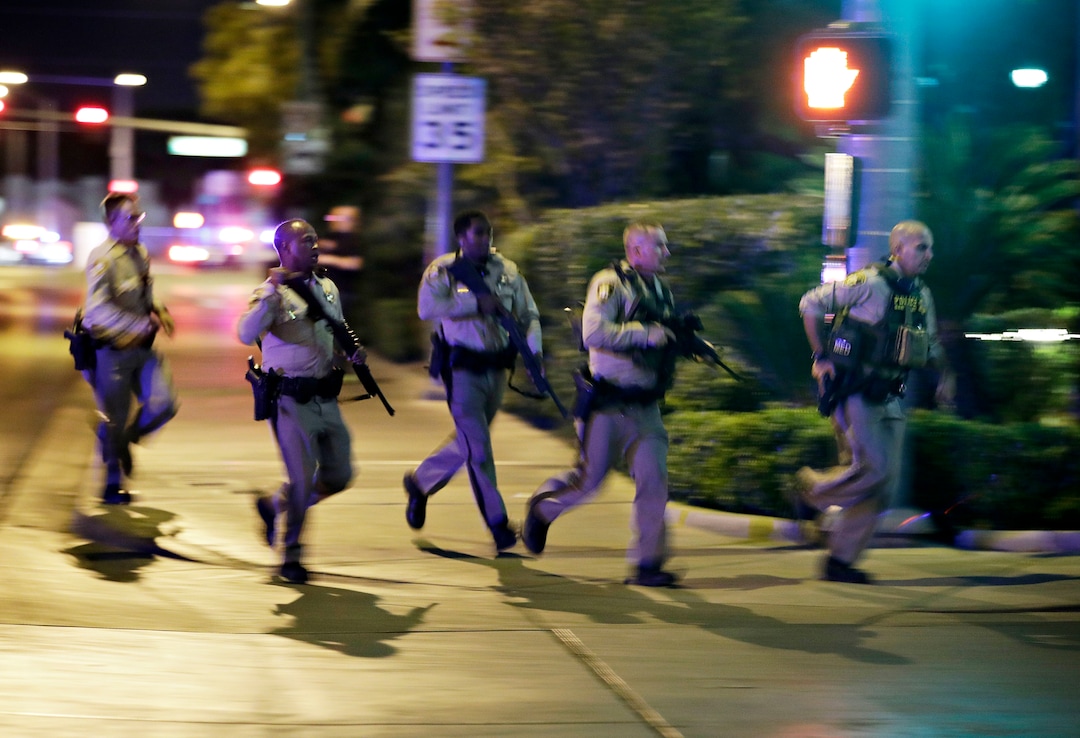 Police run to cover at the scene of a shooting near the Mandalay Bay resort and casino on the Las Vegas Strip, Sunday, Oct. 1, 2017, in Las Vegas. Multiple victims were being transported to hospitals after a shooting late Sunday at a music festival on the Las Vegas Strip. (AP Photo/John Locher)