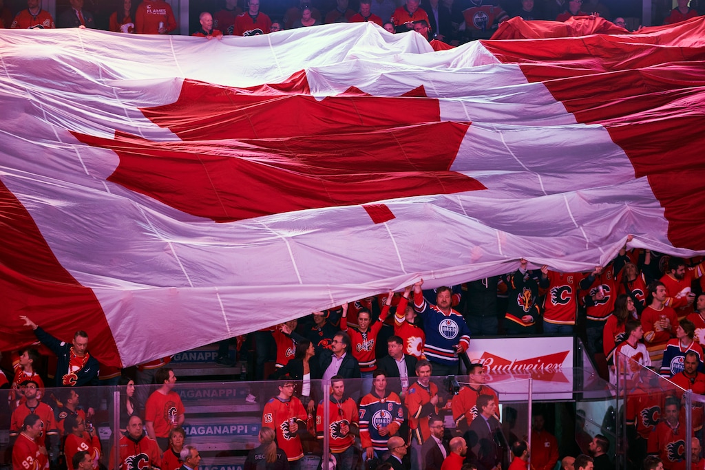 (Todd Korol | The New York Times) Fans hoist a giant Canadian flag during a 2022 hockey game. Thousands of Americans are exploring the prospect of getting Canadian citizenship.
