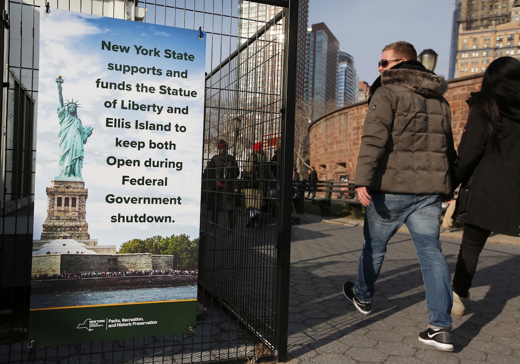 (AP Photo/Seth Wenig) Tourists walk past a sign near the embarkation point for the Statue of Liberty in New York, Thursday, Dec. 27, 2018. The Statue of Liberty and Ellis Island will remain open despite the ongoing partial government shutdown, even as some national parks and monuments close down, according to New York Gov. Andrew Cuomo.