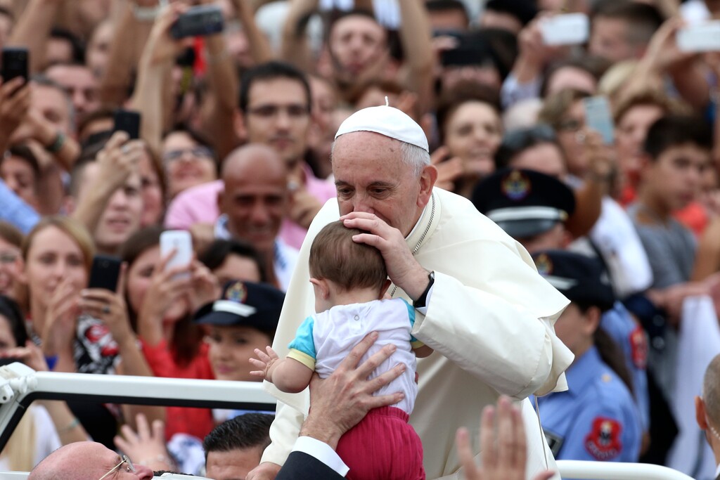 Pope Francis kisses a baby as he is driven through the crowd, in Mother Teresa Square, in Tirana, Sunday, Sept. 21, 2014. Pope Francis arrived Sunday in Albania on his first European trip, designed to highlight the Balkan nation's path from a brutal communist state where religion was banned to a model of Christian-Muslim coexistence for a world witnessing conflict in God's name. (AP Photo/Hector Pustina)