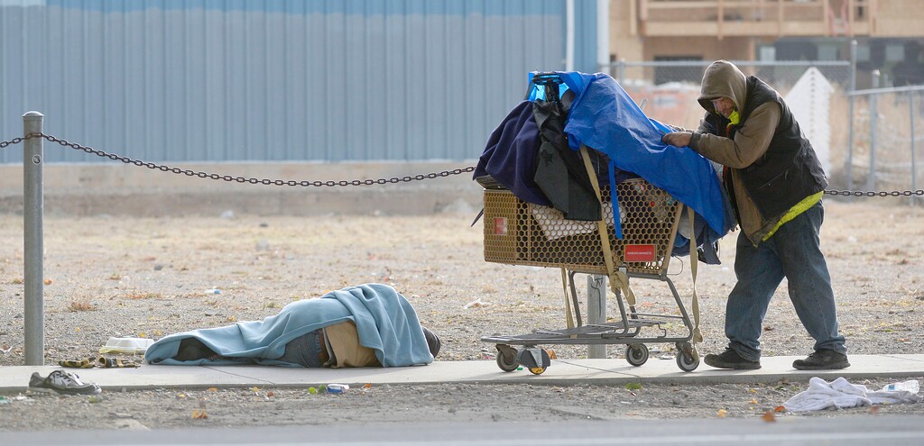 (Al Hartmann  |  Tribune file photo) This 2016 file photo shows a homeless man with his belongings in a shopping cart passing by a man sleeping on the sidewalk along 600 West and 150 South. The Kem Gardner Policy Institute is recommending that Utah appoint a homeless services officer to oversee such efforts statewide to improve communication, coordination and accountability going forward.