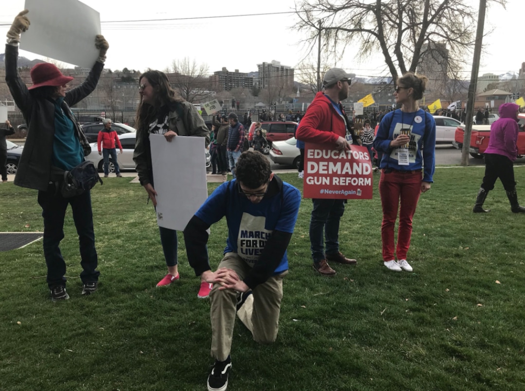 (Lillian Reed | The Salt Lake Tribune) Southern Utah University student Matthew Davis, 23, kneels while pro-gun protestors parade by the March for Our Lives on Saturday, March 24. Davis did not want to share why he kneeled but said he knew people who were hurt in the Las Vegas shooting.