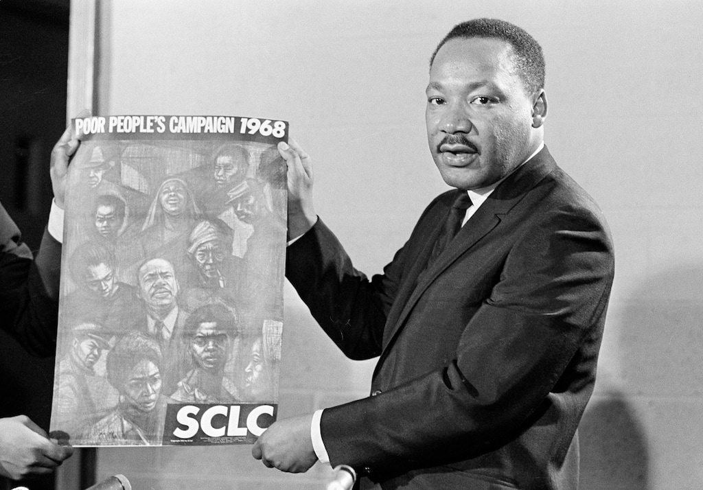 FILE - In this March 4, 1968 file photo, civil rights leader Rev. Dr. Martin Luther King, Jr., president of the Southern Christian Baptist Leadership Conference (SCLC), displays the poster to be used during his Poor People's Campaign this spring and summer of 1968.  Thousands of anti-poverty activists have launched a campaign in recent weeks modeled after Rev. Martin Luther King Jr.'s Poor People's Campaign of 1968. Like the push 50 years ago, advocates are hoping to draw attention to those struggling with deep poverty from Appalachia to the Mississippi Delta, from the American Southwest to California's farm country. (AP Photo/Horace Cort, File)
