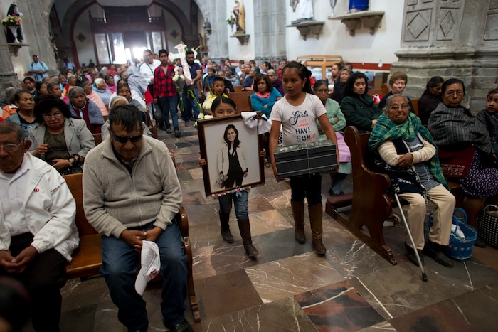 In this Aug. 18, 2017 photo, relatives of murdered doctor and mother, Jessica Sevilla Pedraza, carry a framed portrait of her, a cross, and a box of mementos to be buried alongside her grave, as they arrive for Mass in Villa Cuauhtemoc, Mexico state. Pedraza had been shot in the head and decapitated, and the skin had been flayed from her skull. (AP Photo/Rebecca Blackwell)