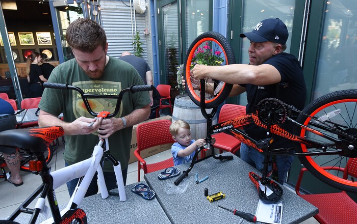 (Francisco Kjolseth  |  The Salt Lake Tribune)  Ryan Nelson, left, joins Rob Carlson and his grandson Jayce Rzepkowski, 4, and other volunteers and workers at Squatter's Pub Brewery as they assemble 80 bicycles on Tuesday, May 29, 2018, at the brewery which will be given away to 1st and 2nd graders at Washington Elementary on Wednesday. Part of the program is backed by the Can'd Aid Foundation.