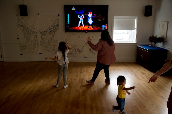 (Jeremy Harmon  |  The Salt Lake Tribune) Seven-year-old Yaretzi plays a dance game with volunteer Tiffany Young at the First Unitarian Church on 1300 East in Salt Lake City on Dec. 14, 2018. Seventeen-month old Bella reaches for the hand of volunteer Easton Smith so she can join in the game.