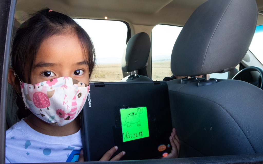 (Megan Marples | Cronkite News) Second-grader Winona Begaye uploads homework in her family’s vehicle near Piñon. Navajo Nation schools have remained virtual this fall because it’s too dangerous to reopen their doors. To help families with no internet or poor access get online, the Piñon Unified School District outfitted school buses with Wi-Fi.
