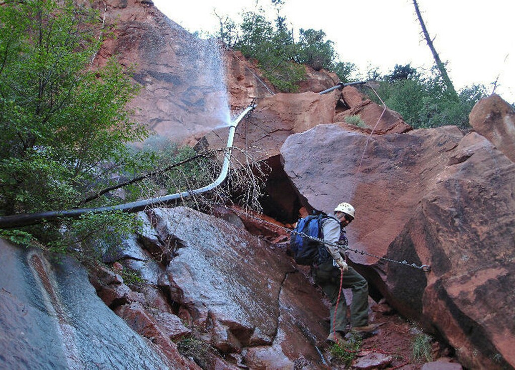 (National Park Service via AP file) In this undated photo provided by the National Park Service shows a water spraying from a break in an exposed section of the Grand Canyon trans-canyon waterline as a worker attempts repairs. Officials have temporarily placed restrictions on water use on the North Rim of Grand Canyon National Park after rockslides caused another pipeline break. The National Park Service announced Thursday, May 23, 2019, that public laundry and shower facilities are closed as well as public restrooms with flushing toilets. The park service says portable toilets are replacing the restrooms. Drinking water remains available for visitors.