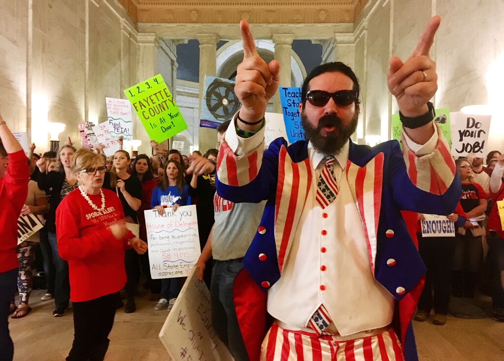 FILE - In this March 1, 2018 file photo, Parry Casto, a fifth grade teacher at the Explorer Academy in Huntington, W.Va., dressed in an Uncle Sam costume leads hundreds of teachers in chants outside the state Senate chambers at the Capitol in Charleston, W.Va  The strike rolled into its second weekend with the state Senate planning to meet Saturday, March 3 after declining to take a vote on whether the teachers will get the 5 percent pay raise negotiated by Gov. Jim Justice and union leaders.  (AP Photo/John Raby)