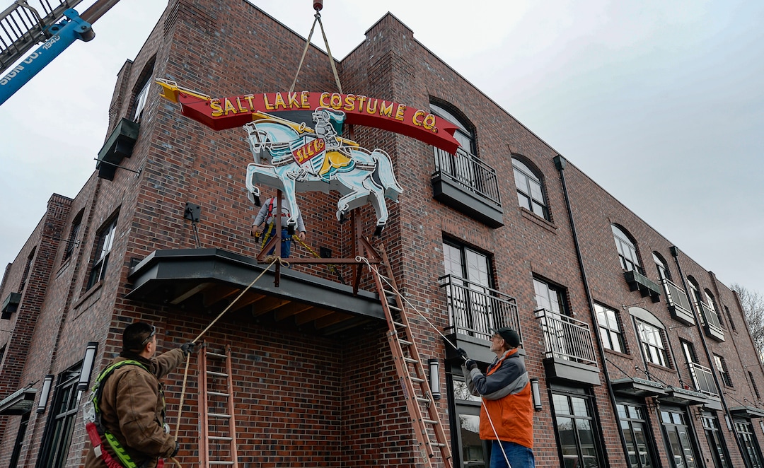 (Francisco Kjolseth  |  The Salt Lake Tribune)  The Salt Lake Costume Co. sign, originally designed by Lloyd S. Coley in the '50s while working for Rainbow Neon Sign Co., lives on once more as Sergio Camacho, left, and Don Fitches help put it back home in its original location at 1700 S. 1100 East on Monday, Dec. 23, 2019, in what is now called the Salt Lake Costume Apartments.