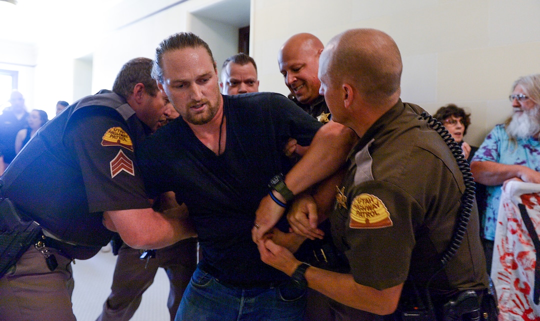 (Leah Hogsten  |  The Salt Lake Tribune) Ethan PetersenÊwithÊCivil Riot, a SLC-basedÊcivilÊresistance collective, and other opponents of the proposed inland port are escorted out of the Utah Inland Port Authority Board meeting by Utah Highway Patrol officers at the Capitol, June 5, 2019. The Inland Port Authority Board had to cancel its meeting last month after a group of protesters took over the meeting. Petersen was arrested.