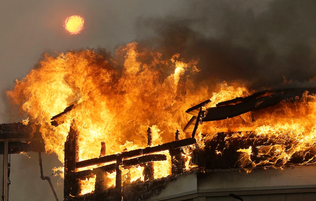 The sun shines above behind a burning building at the Hilton Sonoma Wine Country hotel in Santa Rosa, Calif., Monday, Oct. 9, 2017. Wildfires whipped by powerful winds swept through Northern California sending residents on a headlong flight to safety through smoke and flames as homes burned. (AP Photo/Jeff Chiu)