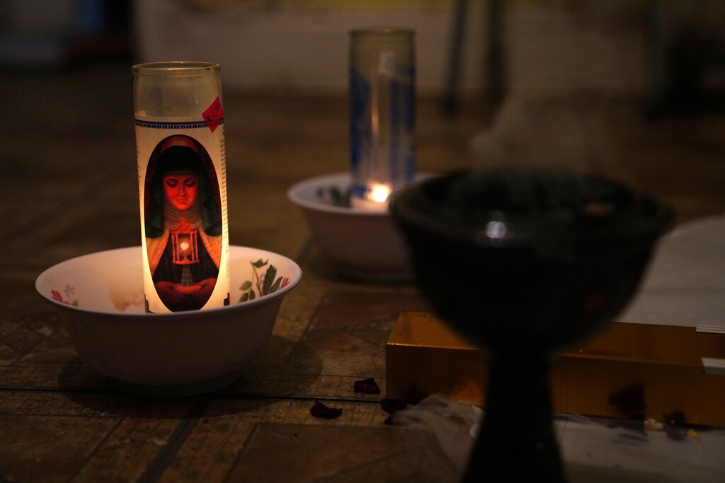 In this May 10, 2020 photo, a candle burns at a makeshift altar for Reyna Martinez's father, who died of COVID-19, in Martinez's home in the Queens borough of New York. Martinez lost both parents to the coronavirus pandemic, which has hit New York's Hispanic population particularly hard. (AP Photo/Emily Leshner)