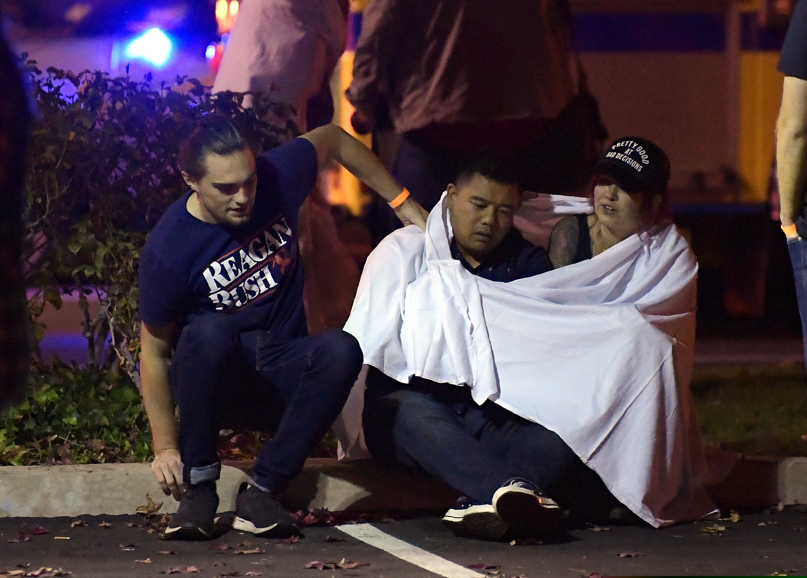 People comfort each other as they sit near the scene Thursday, Nov. 8, 2018, in Thousand Oaks, Calif. where a gunman opened fire Wednesday inside a country dance bar crowded with hundreds of people on "college night," wounding 11 people including a deputy who rushed to the scene. Ventura County sheriff's spokesman says gunman is dead inside the bar. (AP Photo/Mark J. Terrill)