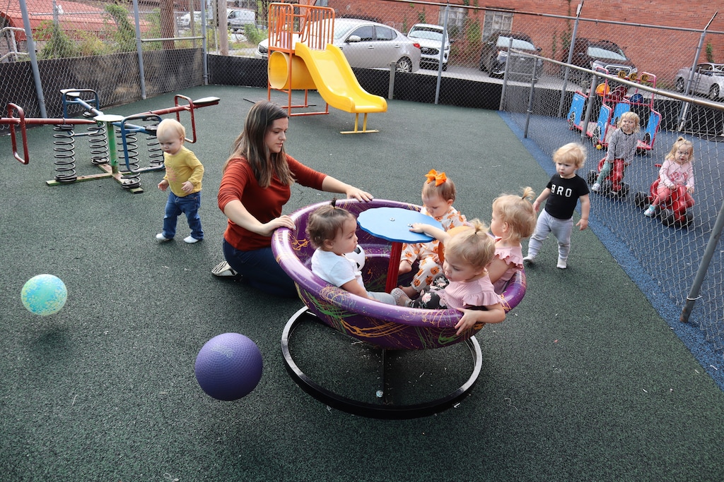 (Leah Willingham | The Associated Press) A daycare staff member pushes toddlers on a teacup merry-go-round playground toy at a West Virginia child care center on Sept. 25, 2023.