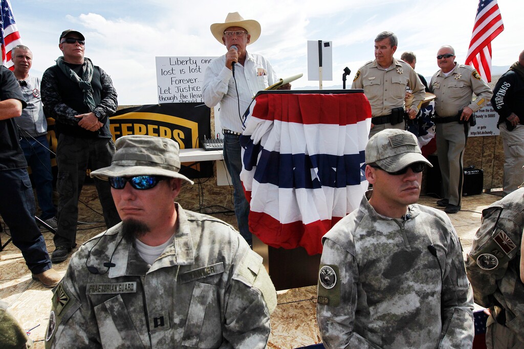 FILE - In this April 12, 2014 file photo, rancher Cliven Bundy, center, addresses his supporters along side Clark County Sheriff Doug Gillespie, right, while being guarded by self-described militia members in the foreground. Twelve of 19 defendants want separate trials in the federal criminal case involving cattleman Cliven Bundy and an armed standoff near his southern Nevada ranch. The 70-year-old state sovereignty figure and three of his sons are among those whose attorneys have filed documents in recent weeks seeking to sever their cases from the rest. (Jason Bean/Las Vegas Review-Journal, via AP, File)