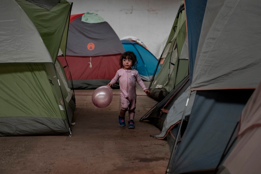 FILE - In this Jan. 2, 2019, file photo, a girl holds a balloon as she walks among tents inside an empty warehouse used as a shelter set up for migrants in downtown Tijuana, Mexico. The Trump administration expects to launch a policy as early as Friday, Jan. 25, 2019, that forces people seeking asylum to wait in Mexico while their cases wind through U.S. courts, an official said, marking one of the most significant changes to the immigration system of Donald Trump's presidency. (AP Photo/Daniel Ochoa de Olza, File)