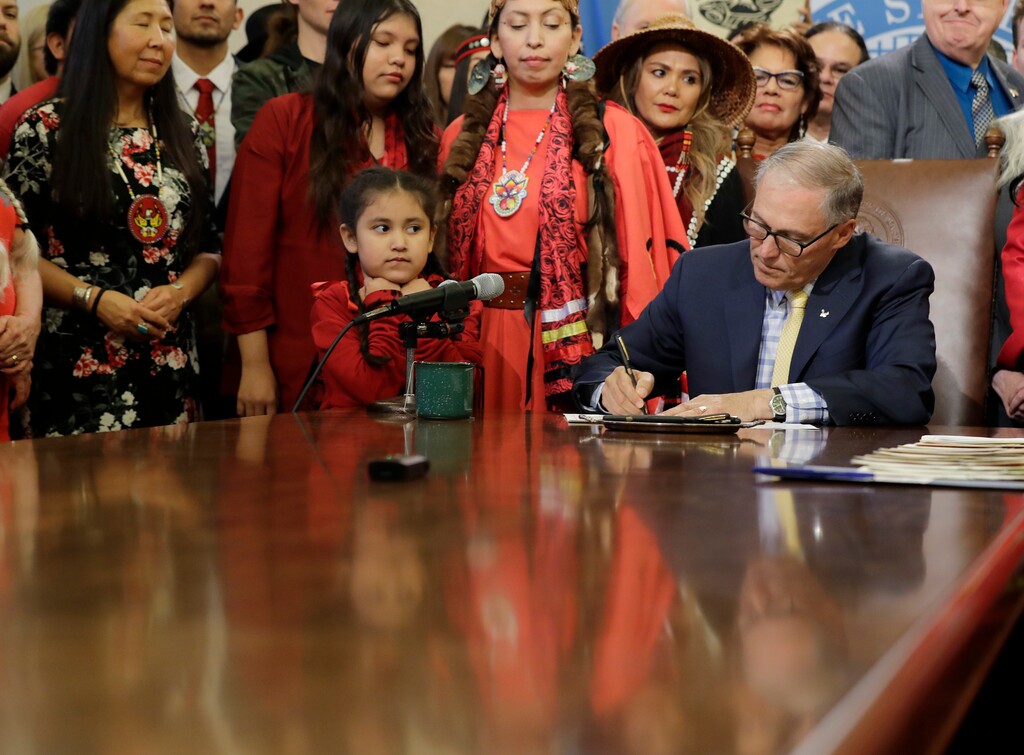 (Ted S. Warren | The Associated Press) Washington Gov. Jay Inslee, lower right, signs a bill into law, Wednesday, April 24, 2019, at the Capitol in Olympia, Wash. The bill creates liaison positions within the Washington State Patrol, and requires the agency to develop best practices in hopes of reducing disproportionate rates of violence faced by Native American and indigenous women, and also the frequency with which perpetrators of the crimes avoid justice. (AP Photo/Ted S. Warren)
