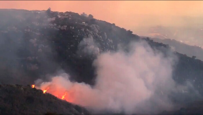 (Mike Eliason | Santa Barbara County Fire Department via AP) In this image taken from video provided by the Santa Barbara County Fire Department, a wind driven spot fire burns on the west side below Gibraltar Road as smoke from a wildfire fills the air in Santa Barbara, Calif., Saturday, Dec. 16, 2017. The Thomas Fire is now the third-largest in California history.