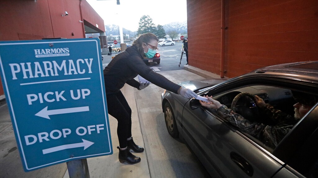 (Rick Bowmer  |  AP file photo) Harmons employee Sarah Kiel gives away a free digital thermometer at the pharmacy drive-thru window Wednesday, April 1, 2020, in Salt Lake City. The grocery chain will require all customers to wear masks.