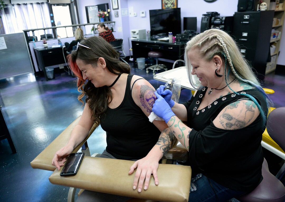 (Al Hartmann  |  The Salt Lake Tribune) 	Terrina Francis, tatoo artist and owner of Fallen Angel Tattoo, is Salt Lake's only all-women tattoo studio.  She works on a personal tattoo for Shannon Gibbs, left.  Gibbs squints in momentary pain as she hits a senstivie part of her arm.   The design is an old-fashioned cameo skull that she has thought about and wanted for four years.   Francis also offers to tattoo over scars and disfigurements due to domestic violence, breast cancer, and burns.   The shop offers a place where women can feel comfortable about getting tattooed in a very male-dominated field. 
