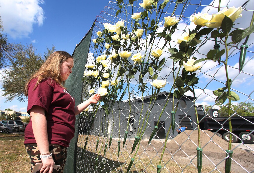 Annabel Claprood, a student at Marjory Stoneman Douglas High School, touches one of the roses at the Pulse nightclub, Wednesday, Feb. 28, 2018, in Orlando, Fla.  Parents and students of Marjory Stoneman Douglas High School made a stop at the site of the nightclub attack on their way back home from Tallahassee. Students returned to class at the high school, Wednesday, following the Feb. 14 mass shooting that killed several students and teachers.  (Red Huber/Orlando Sentinel via AP)