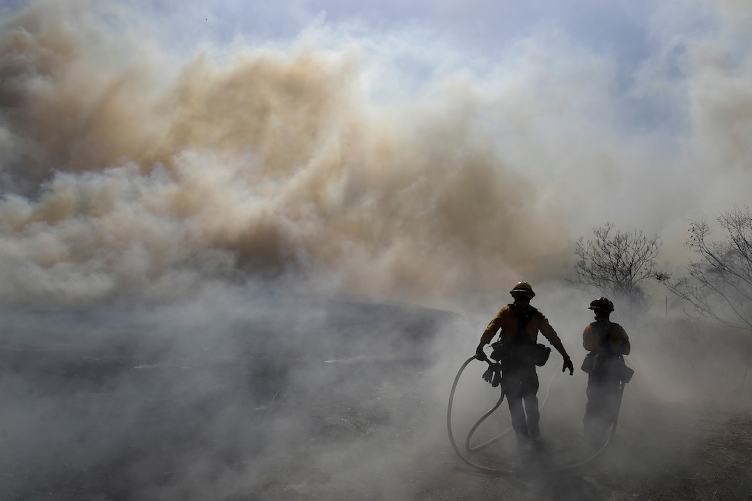 (Marcio Jose Sanchez | AP)  Firefighters walk through a cloud of smoke as winds fuel the Easy Fire Wednesday, Oct. 30, 2019, in Simi Valley, Calif. Fire officials say they're investigating the cause of the fire.