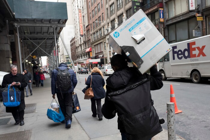 In this Wednesday, Dec. 20, 2017, photo, a delivery man carries a customer order as he leaves the Amazon Prime warehouse in New York. (AP Photo/Mark Lennihan)