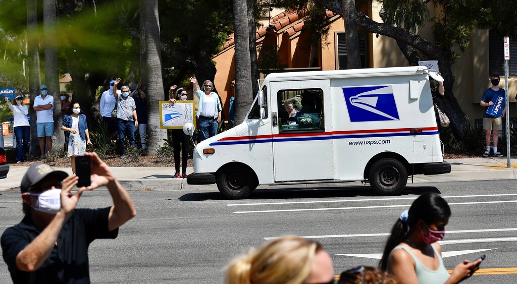 (Jeff Gritchen | The Orange County Register via AP)  A postal carrier drives past protesters during a rally against changes to the United States Postal Service, in Newport Beach, Calif., Tuesday, Aug., 18, 2020.
