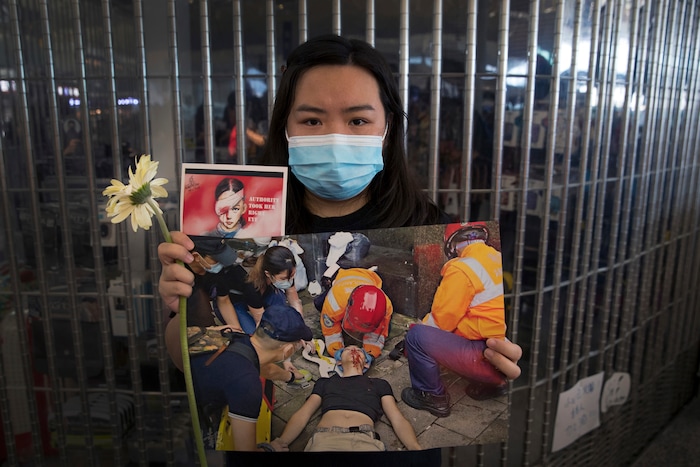 (Vincent Thian | AP Photo) A woman holds a flower and posters showing people injured by police as protesters stage a sit-in rally at he Hong Kong International Airport in Hong Kong, Tuesday, Aug. 13, 2019. Protesters clogged the departure area at Hong Kong's reopened airport Tuesday, a day after they forced one of the world's busiest transport hubs to shut down entirely amid their calls for an independent inquiry into alleged police abuse.